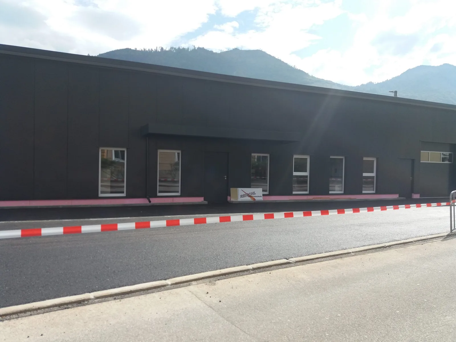 Neues dunkles Firmengebäude mit Fensterreihe an einer Straße, dahinter Berge