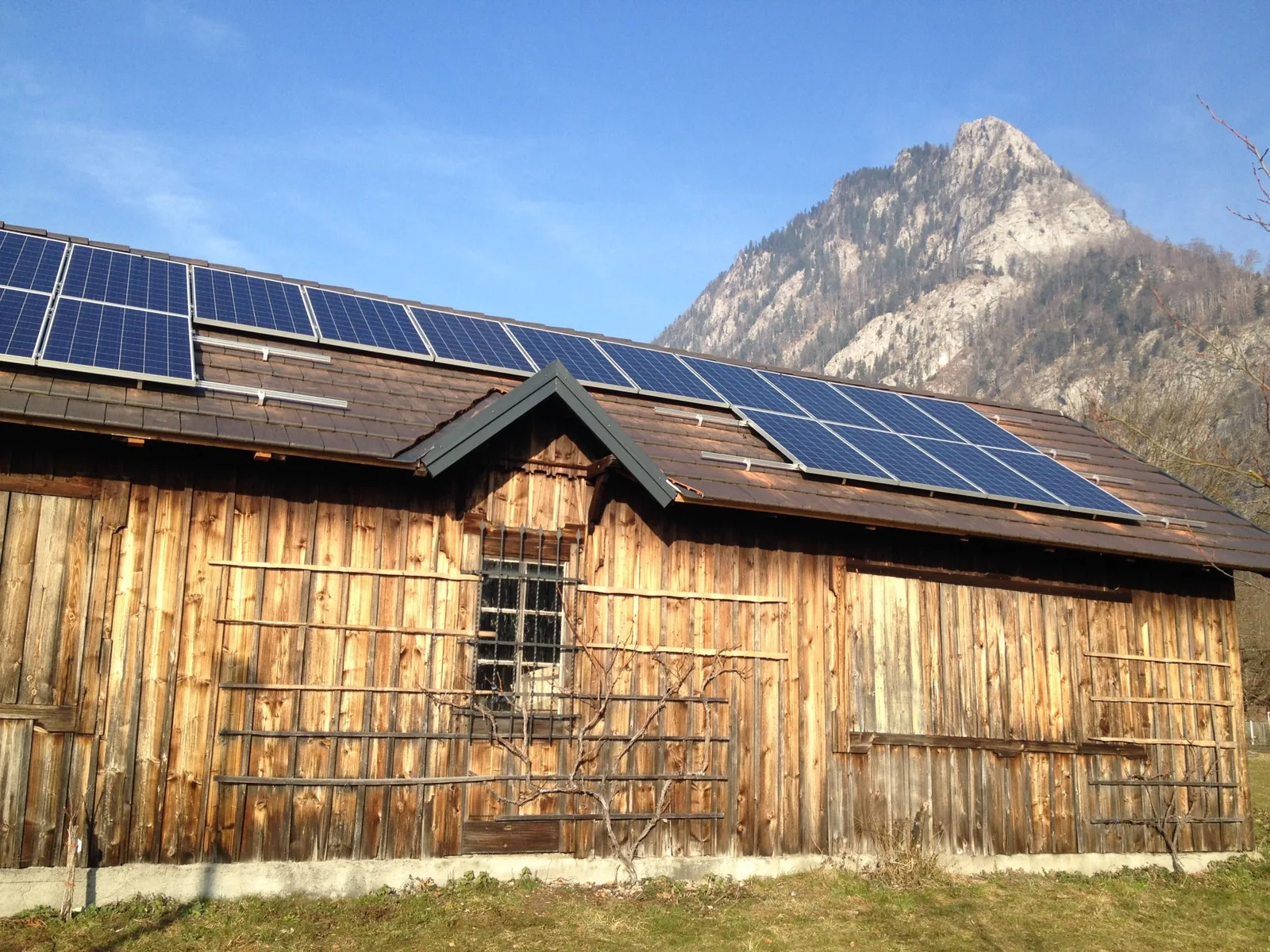 Fertige Photovoltaik-Anlage auf dem Dach eines alten Holzstadels, dahinter ein Berg