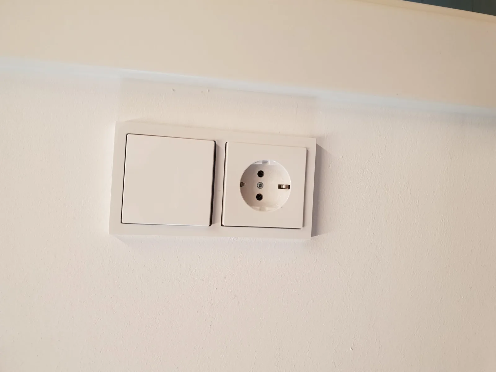 Weißer Lichtschalter und Steckdose in einem gemeinsamen Rahmen an einer hellen Wand